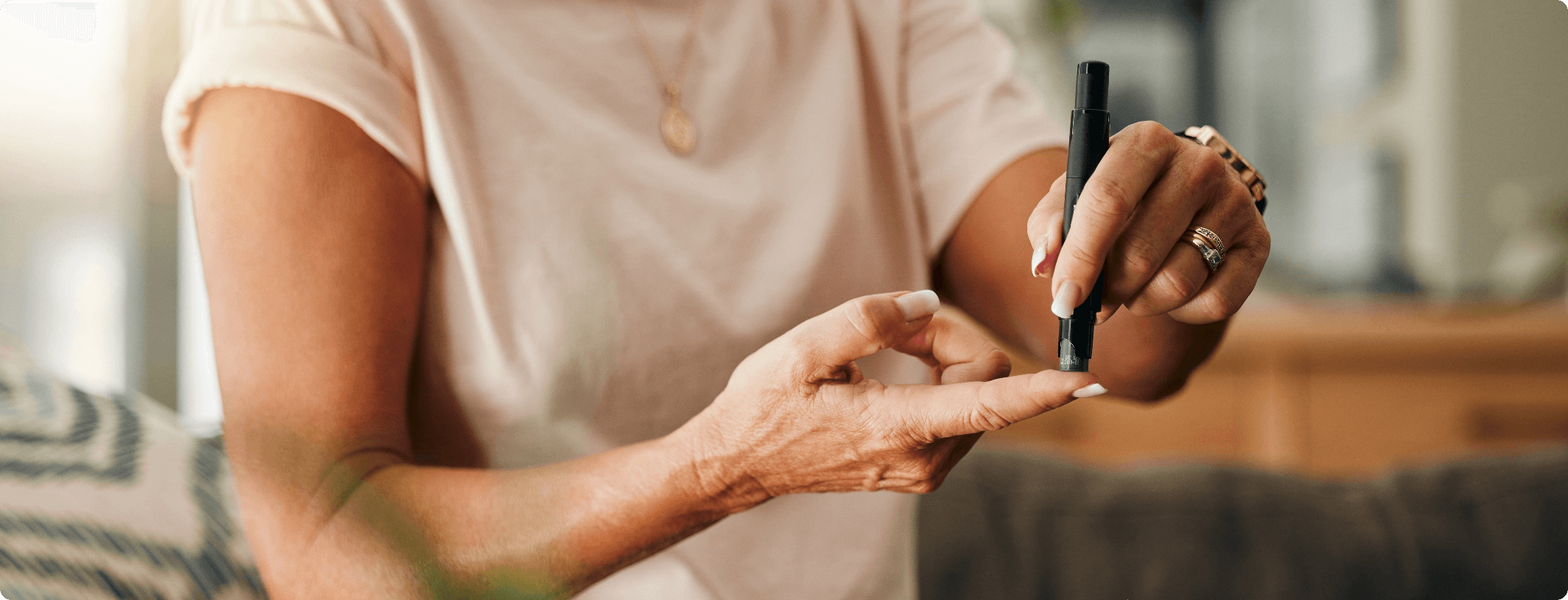 Woman using a lancet device to perform a finger prick blood glucose test on herself at home