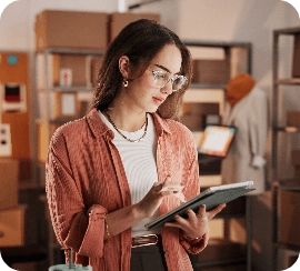 Young woman wearing glasses using a tablet in a warehouse or stockroom environment, representing digital inventory or business management