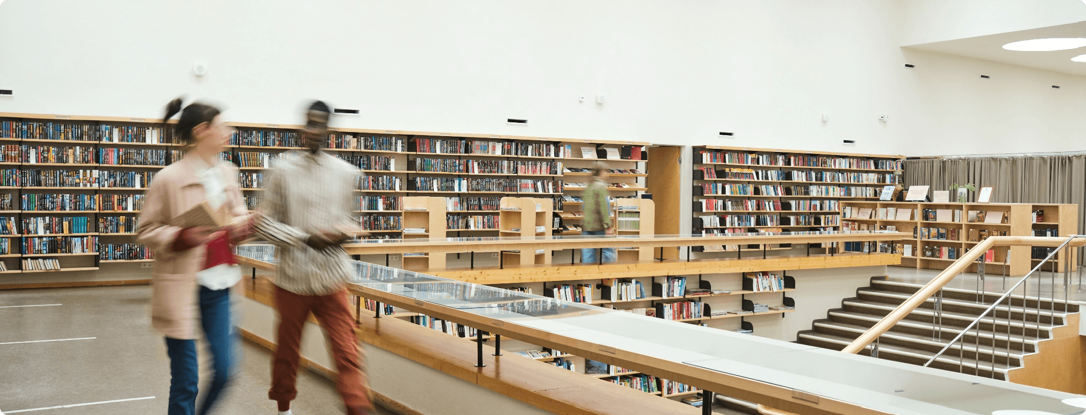 Two people walking through a bright modern library with motion blur, surrounded by extensive floor-to-ceiling bookshelves on multiple levels