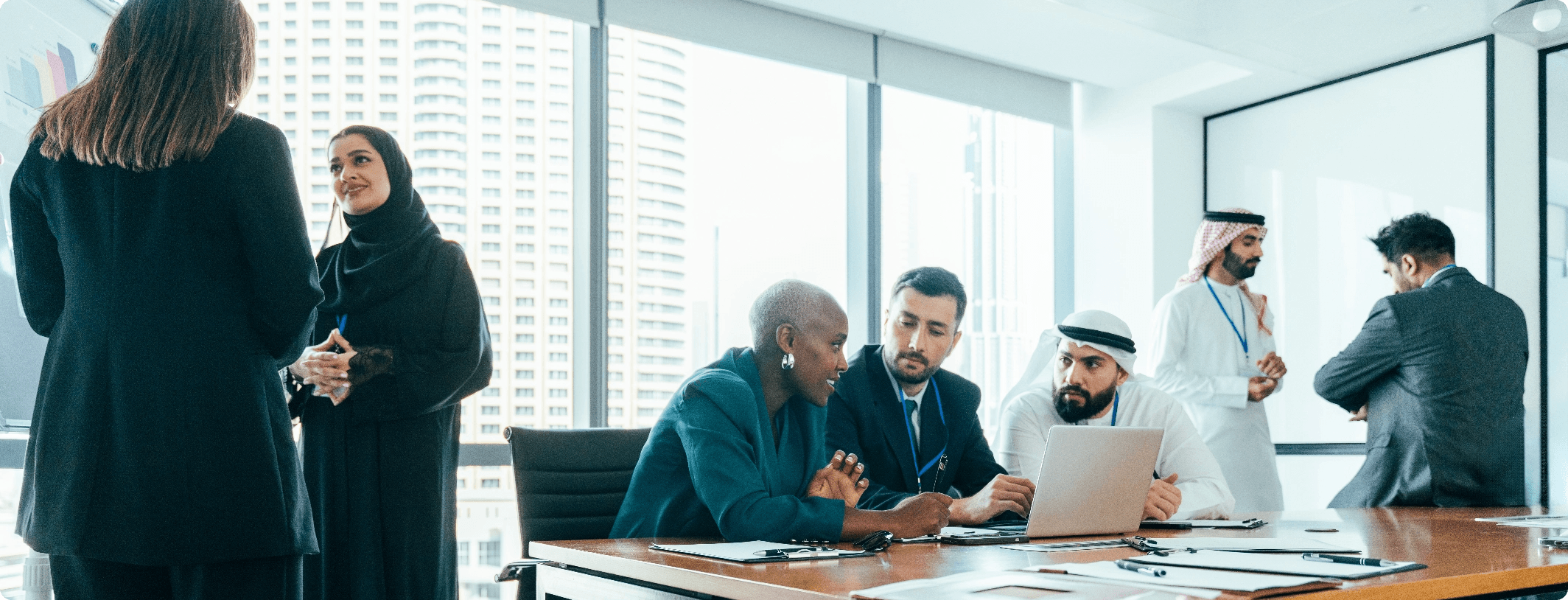 Diverse international business team collaborating around a conference table with laptops in a bright high-rise Dubai office boardroom